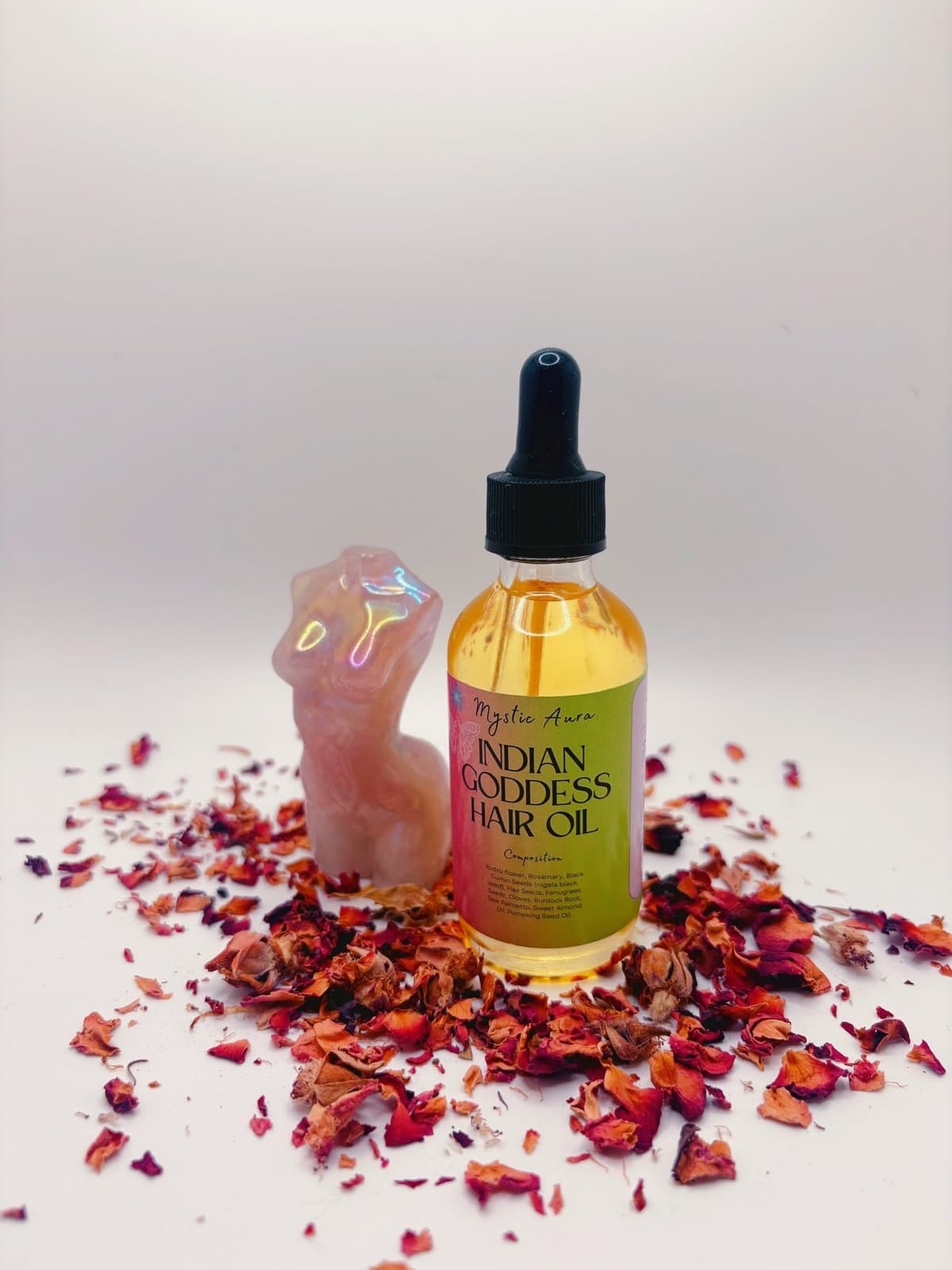 Indian Goddess Hair Oil beside a rose quartz figure, surrounded by rose petals